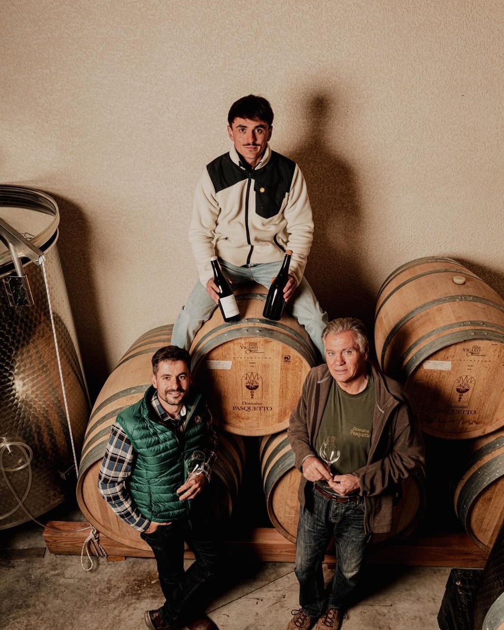 Three men seated on barrels at Domaine Pasquetto
