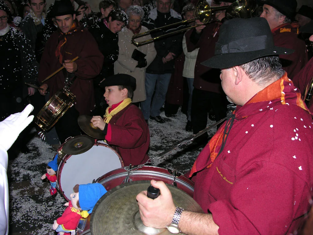 Carnival musicians playing drums and trombone amid a crowd and scattered confetti.